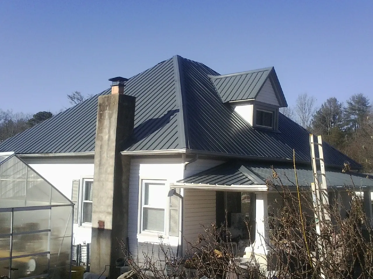 Dark blue standing seam metal roof on a white farmhouse with dormer — Slate & Tile Roof Repair by Roofing Brothers in Wolverton