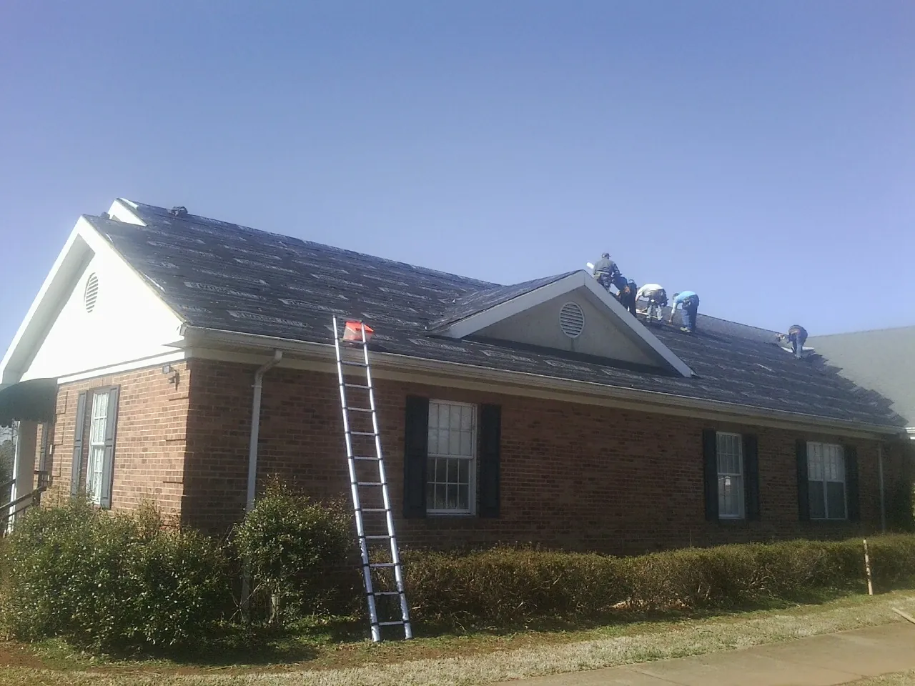 Crew tearing shingles off a brick ranch roof with a ladder set — Emergency Roof Repair work by our crew in Wolverton