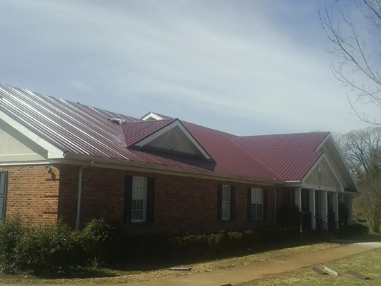 Red metal roof with gabled entries on a long brick building, from a Hail Damage Roof Repair job in Wolverton