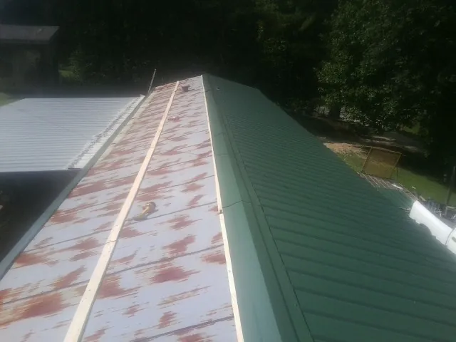 Old rusted panels beside newly installed green metal roofing — Wind Damage Roof Repair by Roofing Brothers in Wolverton