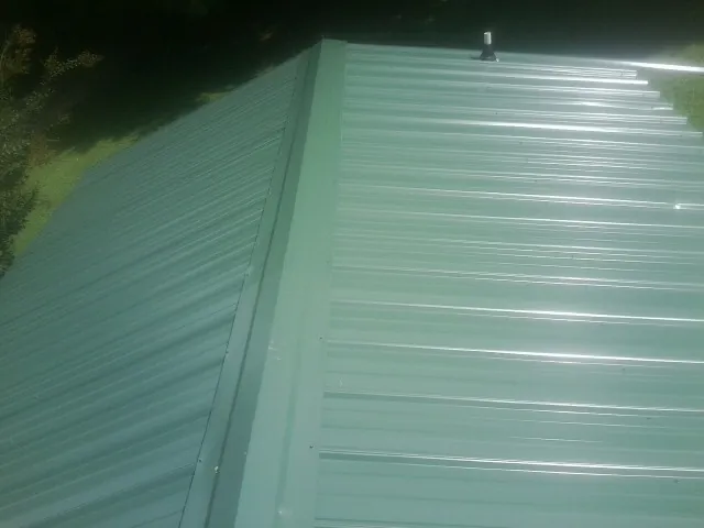 New green metal panels meeting at the ridge of a roof — Flat Roof Repair work by our crew in Wolverton
