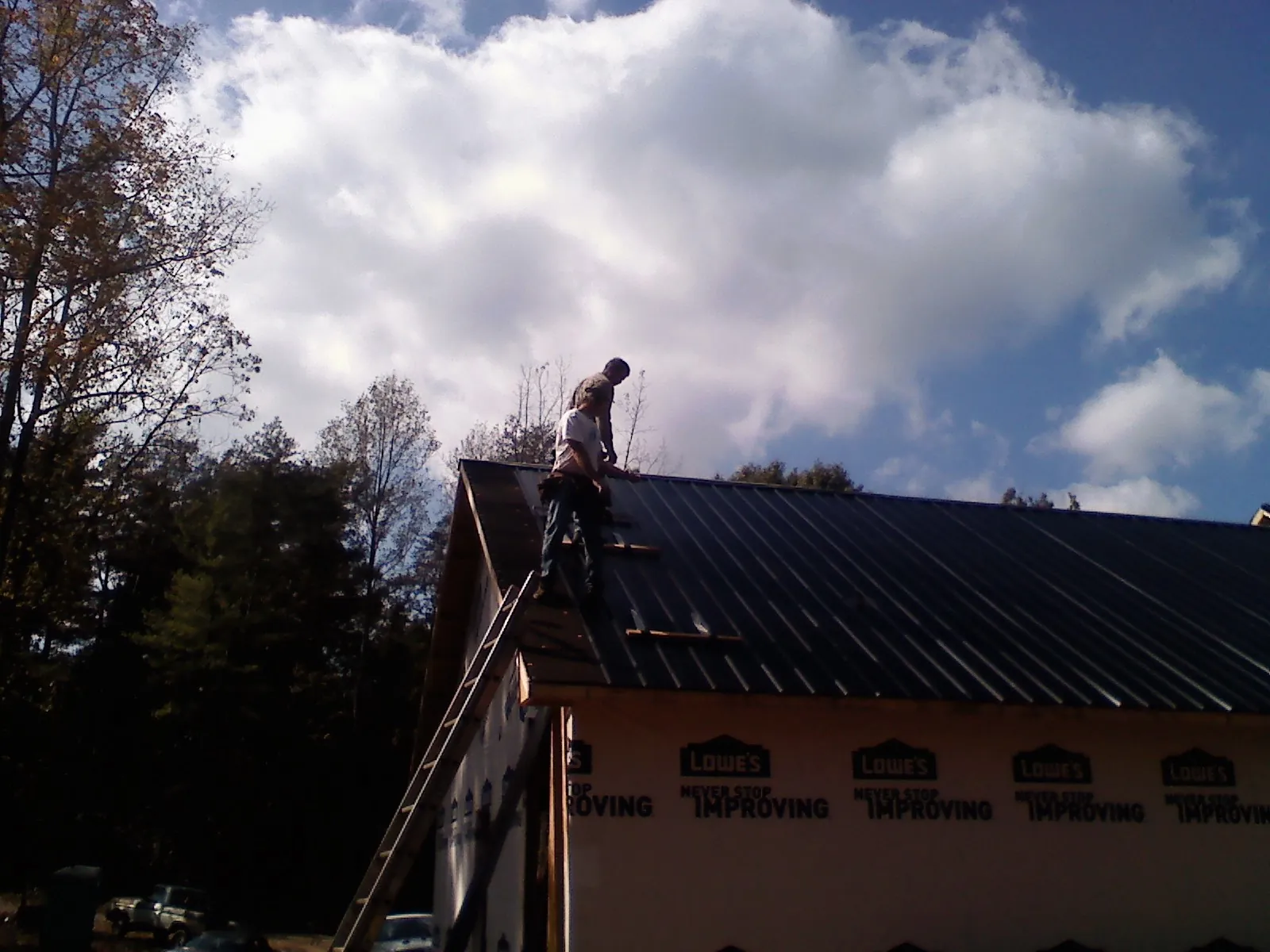 Roofer fastening dark metal panels high against a cloudy sky, from a Roof Inspection job in Wolverton