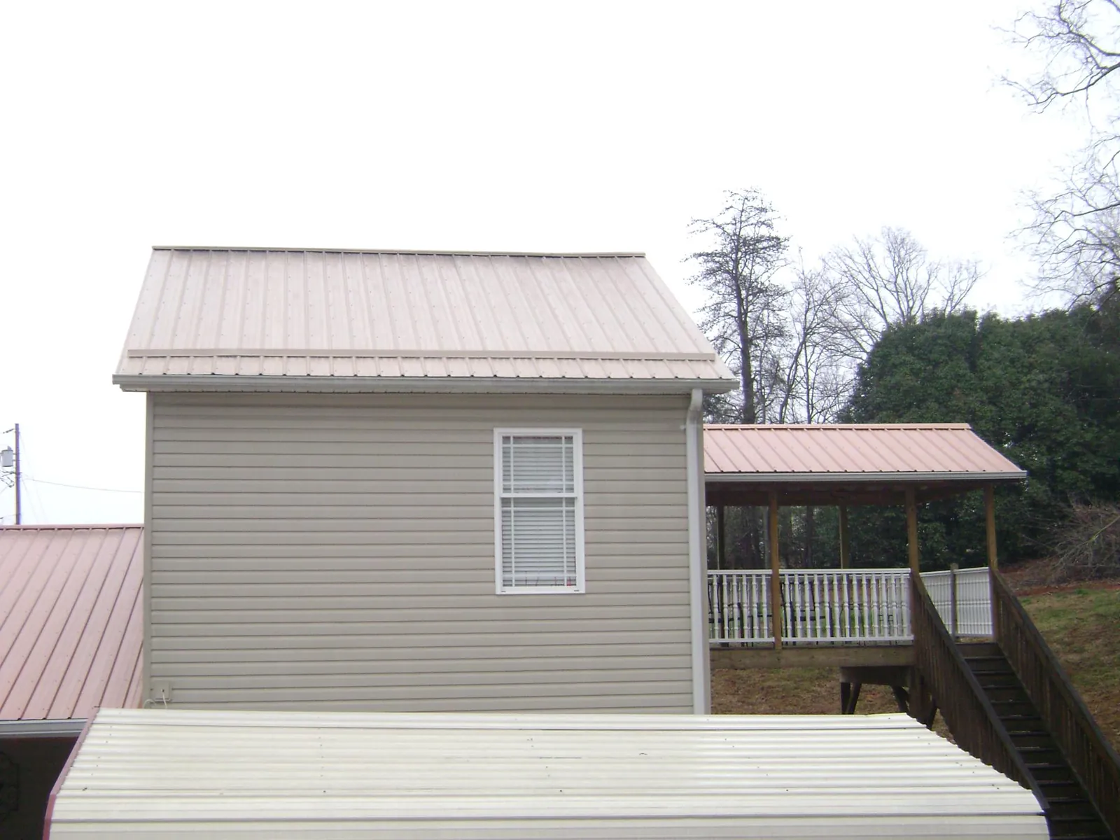Tan metal roofs on a two story addition and attached porch, from a Roof Replacement job in Wolverton